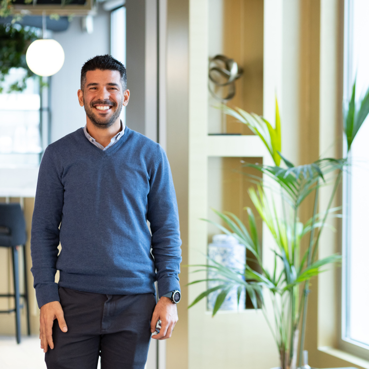 A man smiling, stood in a modern office